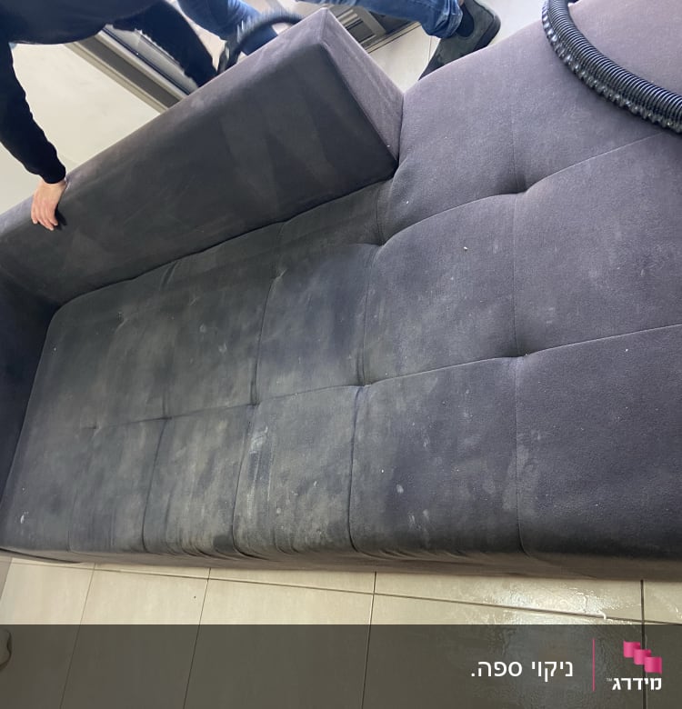 אדם מנקה ספה כהה עם שואב אבק